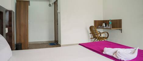 A hotel room with a bed, a wooden wardrobe, a bathroom with a shower, and a small seating area with a chair.