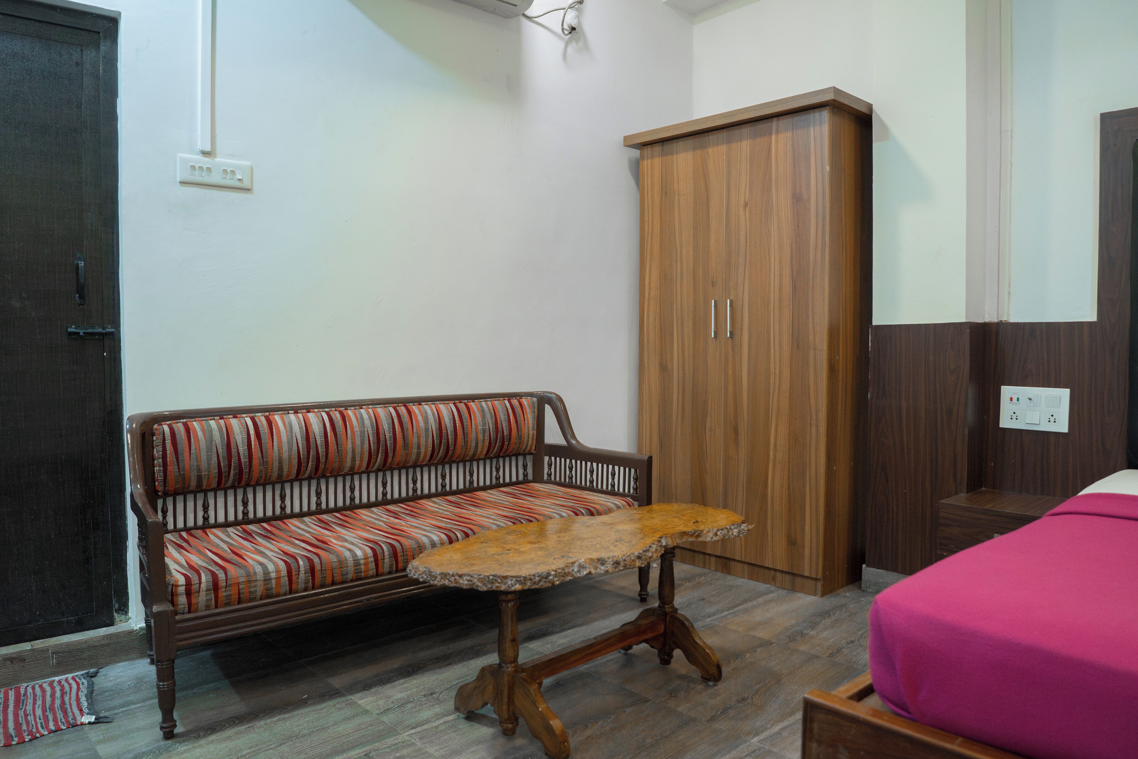 Una habitación con un banco de madera, una pequeña mesa de madera, un armario y una cama con edredón rosa.