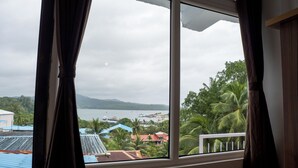 A view from a window with curtains, overlooking a coastal area with buildings, palm trees, and a body of water. - Ocean View (Port Blair)