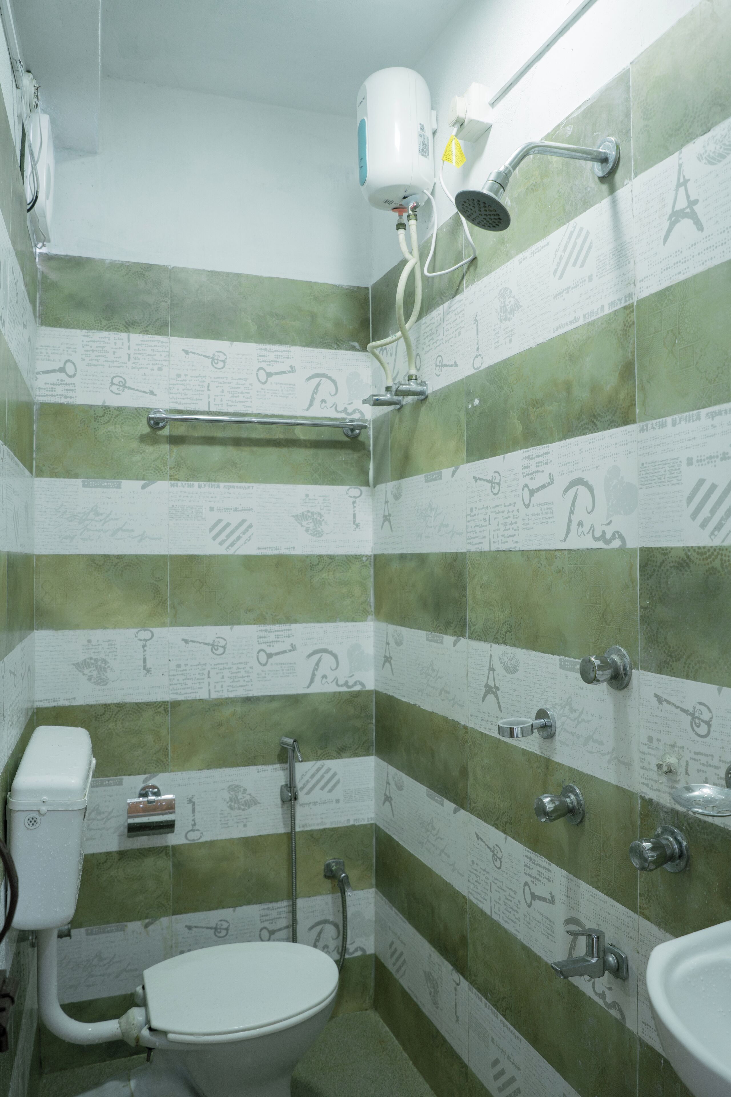 Un baño con baldosas verde y blanco a rayas, un inodoro blanco, un lavabo y una ducha con cabezal de ducha manual.