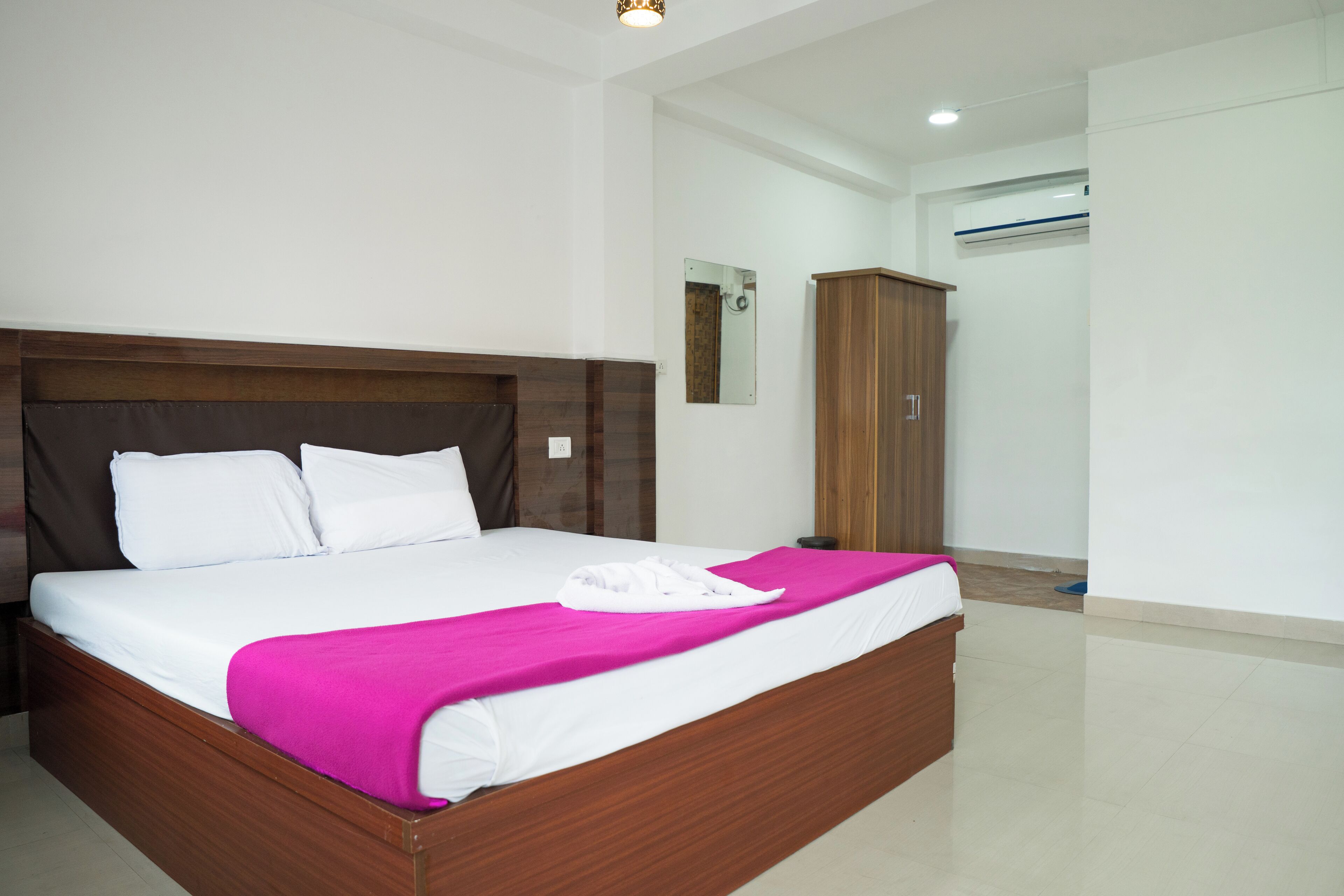 Una cama bien hecha con cabecera de madera, una manta rosa brillante y ropa de cama blanca.