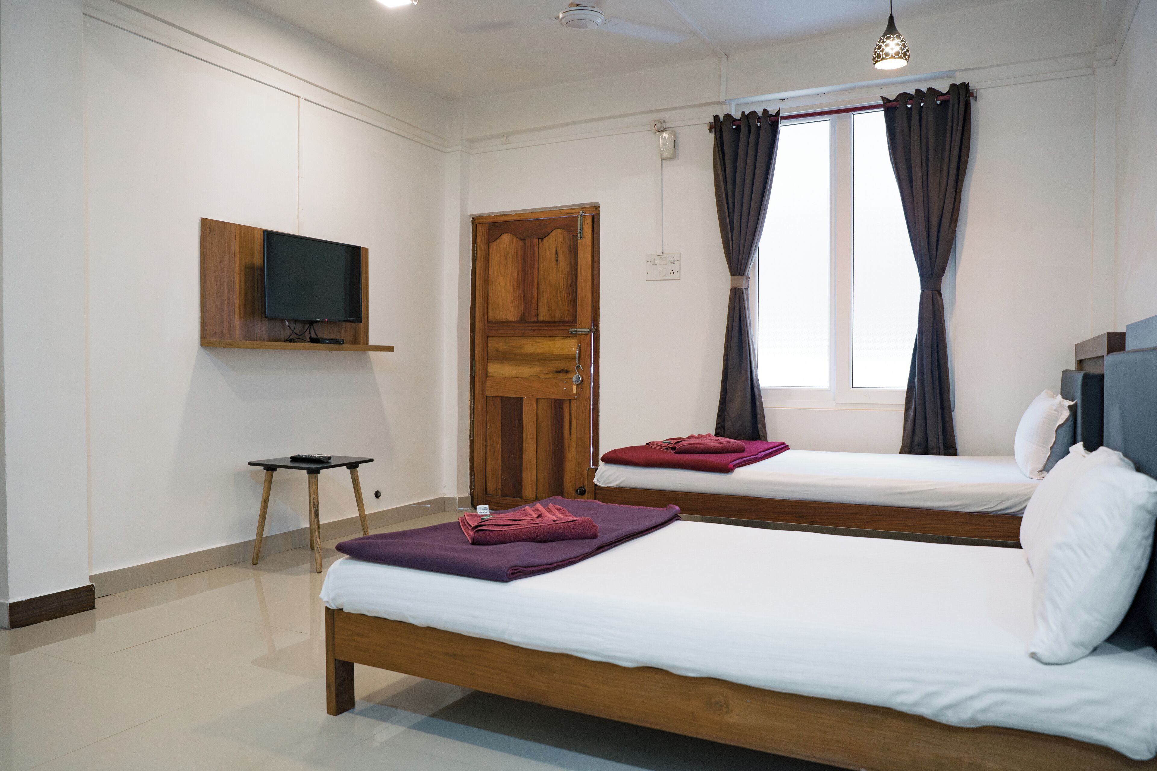 A modern hotel room with two wooden beds, a flat-screen TV mounted on the wall, and a small table.