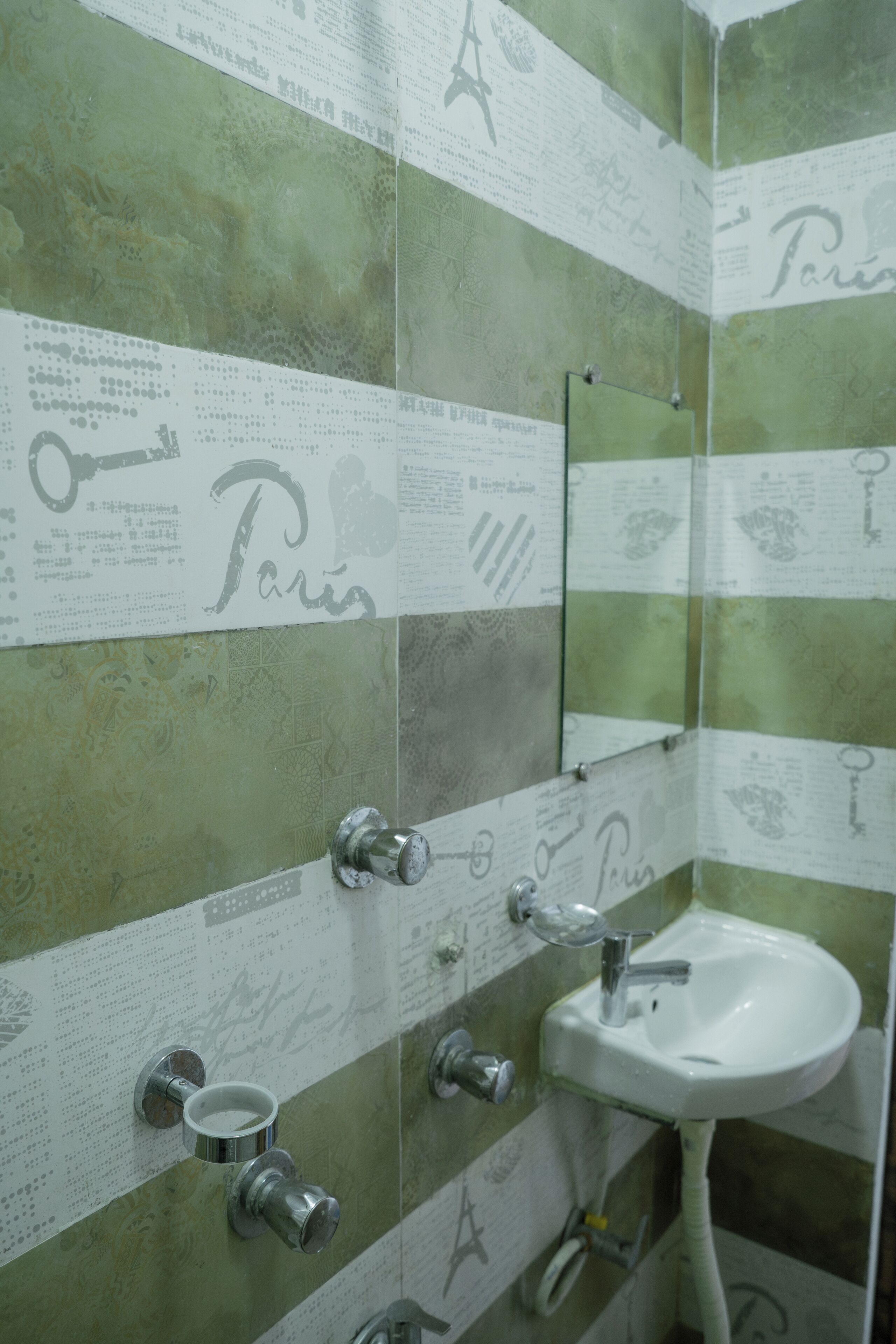 Une salle de bain avec des carreaux verts à motifs, un lavabo blanc et un miroir.