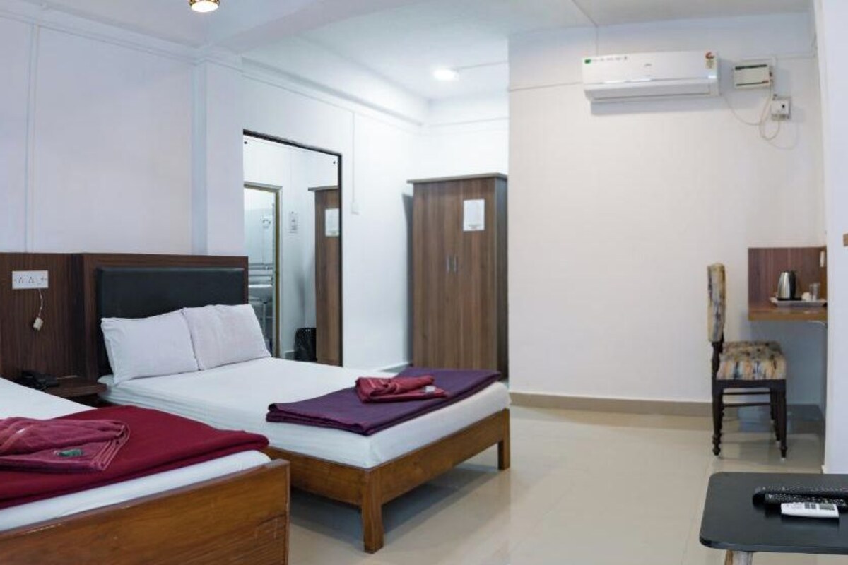 A hotel room with two beds, a small table, a TV, and a wardrobe.