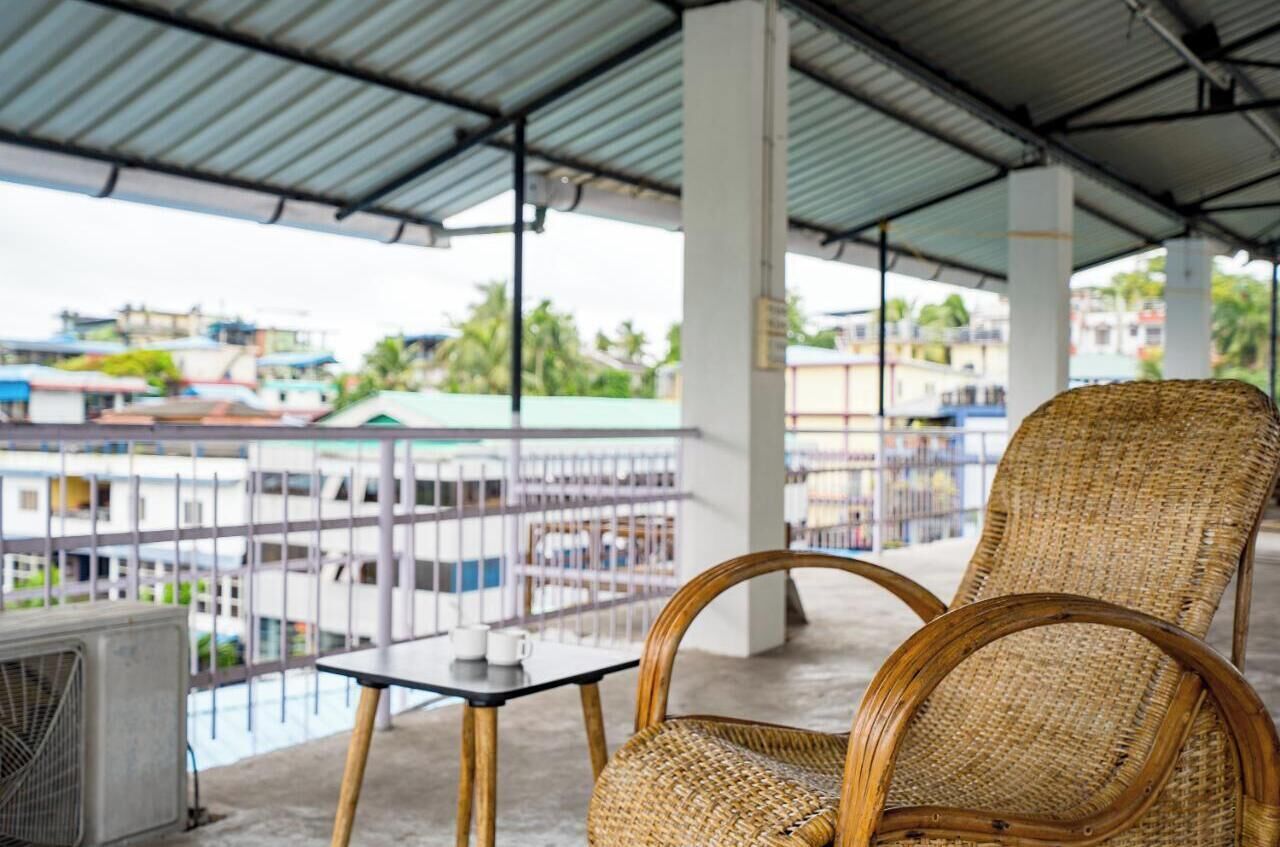 A wicker chair and table on a balcony with a view of buildings and a fence.