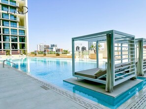 Ein moderner Poolbereich mit einer gläsernen Lounge, klarem, blauem Wasser und einer Skyline im Hintergrund.