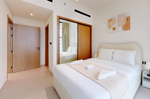 A hotel room with a large bed, a wooden door, a mirror, and a nightstand with a lamp.