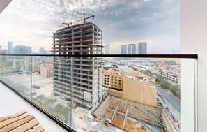 A high-rise building under construction with a view of a cityscape through a glass balcony.