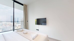 Hotellihuone, jossa on suuri sänky, seinälle asennettu televisio ja suuri ikkuna, josta avautuu näkymä kaupungin ylle.