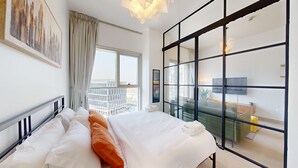 Una habitación de hotel moderna con una cama grande, vista de la ciudad a través de ventanales del suelo al techo y una lámpara contemporánea.