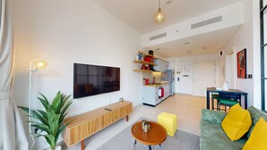 Una sala de estar moderna con televisor de pantalla plana, consola de madera y un otoman amarillo.