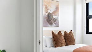 A bedroom with a bed, pillows, a painting, and a window.