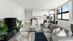 A modern living room with a grey sofa, a flat-screen TV, and a glass coffee table.