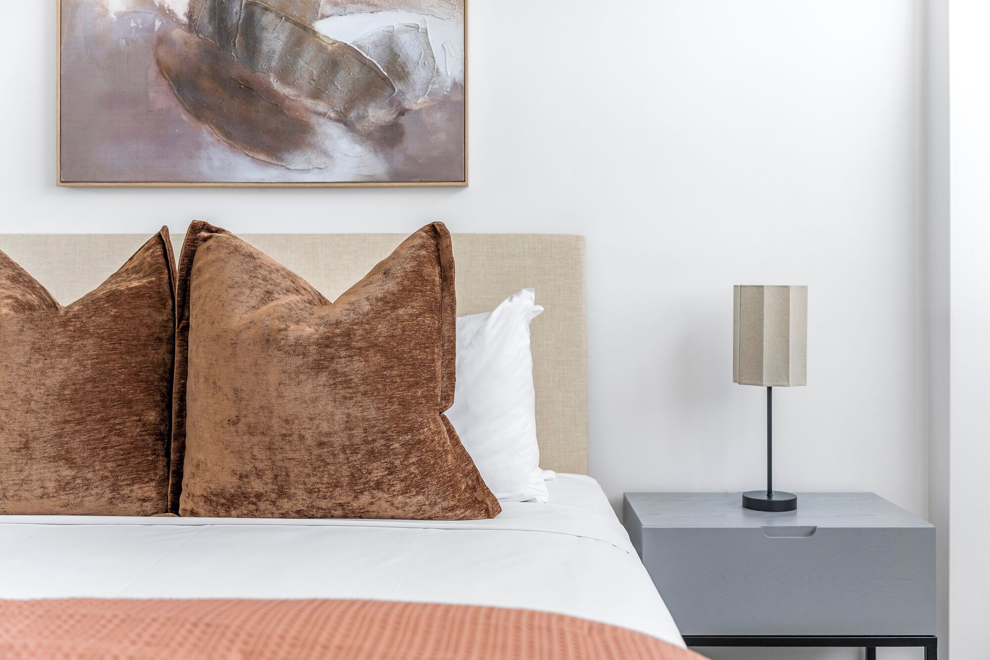 A neatly made bed with two large, textured pillows, a bedside lamp, and a small gray nightstand.