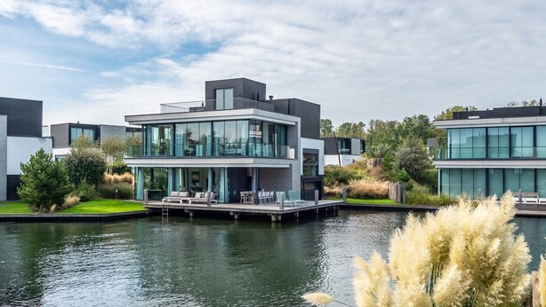 Un moderno edificio residencial de varios pisos con amplias ventanas, un balcón y un muelle que se adentra en el agua.
