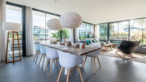 Un comedor moderno con una mesa grande, sillas blancas y vistas a un paisaje urbano a través de amplios ventanales.