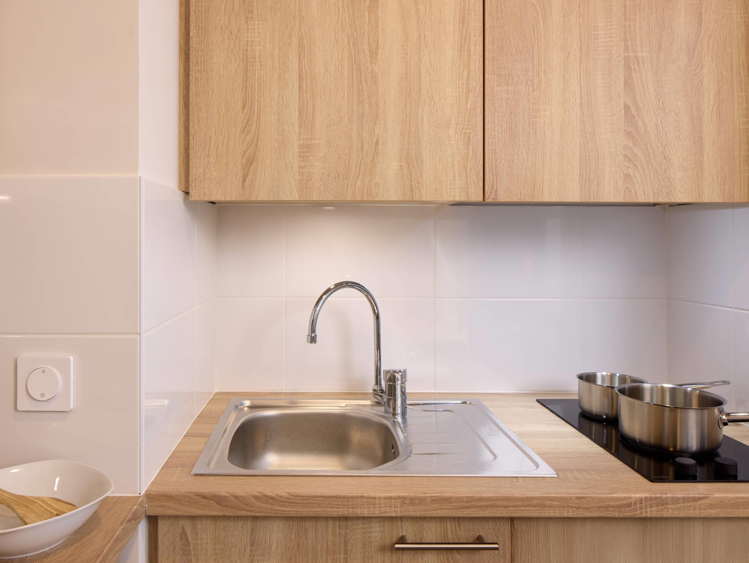 A kitchen with a stainless steel sink, wooden cabinets, and a black induction cooktop.