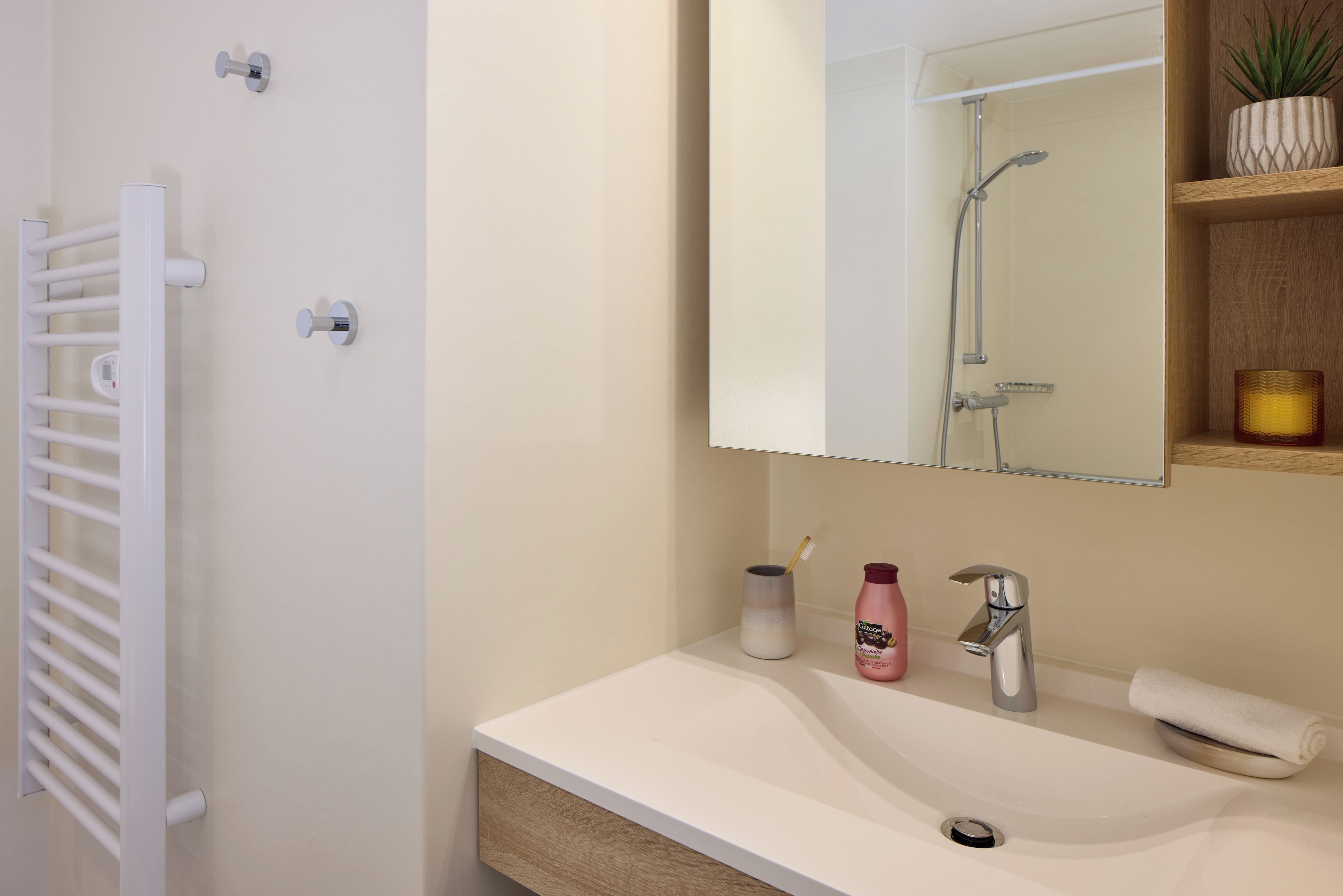 Une salle de bain moderne avec un lavabo blanc, un miroir, une serviette et une douche.