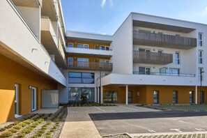 A modern multi-story residential building with balconies, a parking area, and a landscaped garden. - Quality Aparthotel Plerin Saint-Brieuc (Plérin)