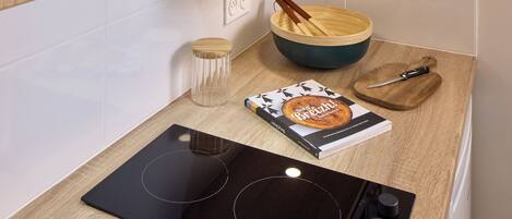 Une cuisine compacte avec des meubles en bois, une plaque de cuisson à induction noire, un four à micro-ondes et un bol accompagné d’une cuillère en bois.