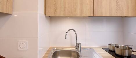 A kitchen with a stainless steel sink, wooden cabinets, and a bowl with a wooden spoon.