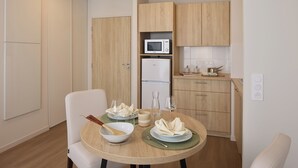 Een kleine keuken met houten kastjes, een magnetron en een koelkast. Er is een eettafel met borden, glazen en een kom.