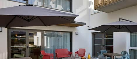 An outdoor patio area with tables and chairs, large umbrellas, and a wooden balcony railing.