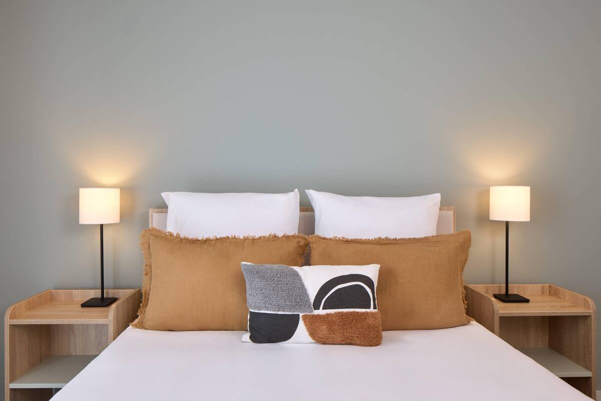 A neatly made bed with white linens and two bedside lamps on wooden nightstands.