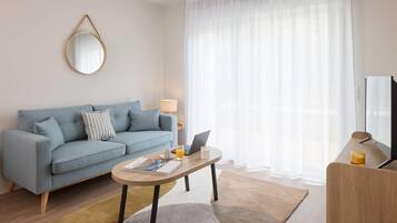 Un salon moderne avec un canapé bleu clair, une table basse ronde et un téléviseur posé sur un meuble en bois.