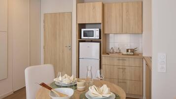 A compact kitchen with a microwave, refrigerator, and wooden cabinets. A dining table with plates, glasses, and a bowl is set for two.