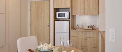 Una cocina compacta con microondas, refrigerador y gabinetes de madera. Una mesa de comedor con platos, vasos y un tazón dispuesta para dos comensales.