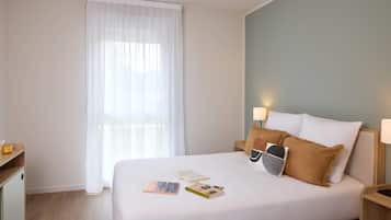 Una camera d'albergo ordinata con un letto, comodini, una scrivania e una finestra con tende leggere.