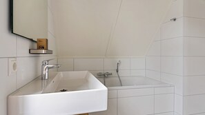 A modern bathroom with a white sink, a mirror, and a shower. - Detached six-person home (Opperdoes)