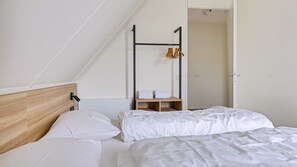 A bedroom with a sloped ceiling, a wooden headboard, two beds with white bedding, a wooden bench with towels, and a clothing rack. - Detached six-person home (Opperdoes)