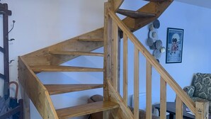 Una escalera de caracol de madera con barandilla, un perchero y un cuadro en la pared.