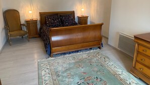 Un dormitorio con una cama de madera, un tapete floral, una silla y mesitas de noche con lámparas.