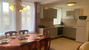 Una cocina compacta con zona de comedor, que presenta un mantel a cuadros, sillas de madera y electrodomésticos básicos.