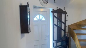 Un pasillo con una puerta blanca, una escalera de madera, un reloj y un radiador.