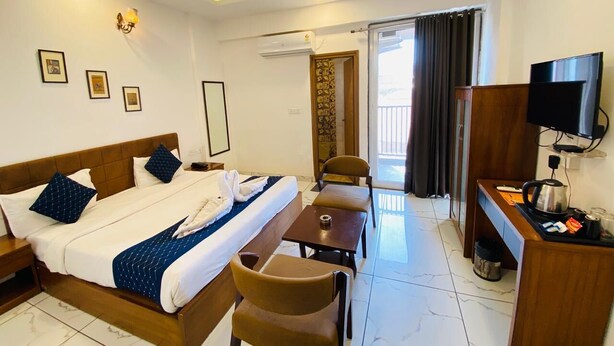A hotel room with a bed, a desk, a chair, a television, and a balcony with curtains. - Hotel Nikanshvee (Udaipur)