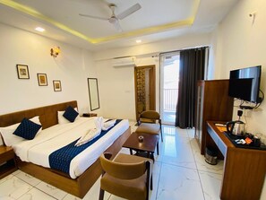 A hotel room with a bed, a desk, a chair, a television, and a balcony with curtains. - Hotel Nikanshvee (Udaipur)