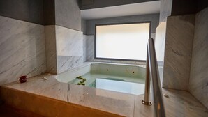 A modern bathroom with a marble bathtub, a small red container, and a window above the tub. - 
THE RIAD PEARL OF MARRAKECH (Jdid)