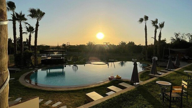 A swimming pool with lounge chairs and umbrellas, surrounded by palm trees and a sunset view. - 
THE RIAD PEARL OF MARRAKECH (Jdid)