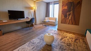 A modern hotel room with a flat-screen TV, a desk, a chair, a sofa, a lamp, a large painting, and a decorative vase. - 
THE RIAD PEARL OF MARRAKECH (Jdid)