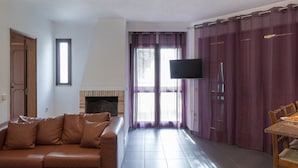 Ein Wohnzimmer mit braunem Ledersofa, einem flachbildfernseher an der Wand, einem Kamin und violetten Vorhängen.