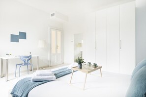 A modern bedroom with a bed, bedside table, chair, wardrobe, and a desk with a chair.