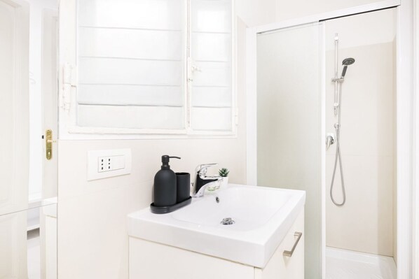 A bathroom with a white sink, a black soap dispenser, a small potted plant, and a shower.