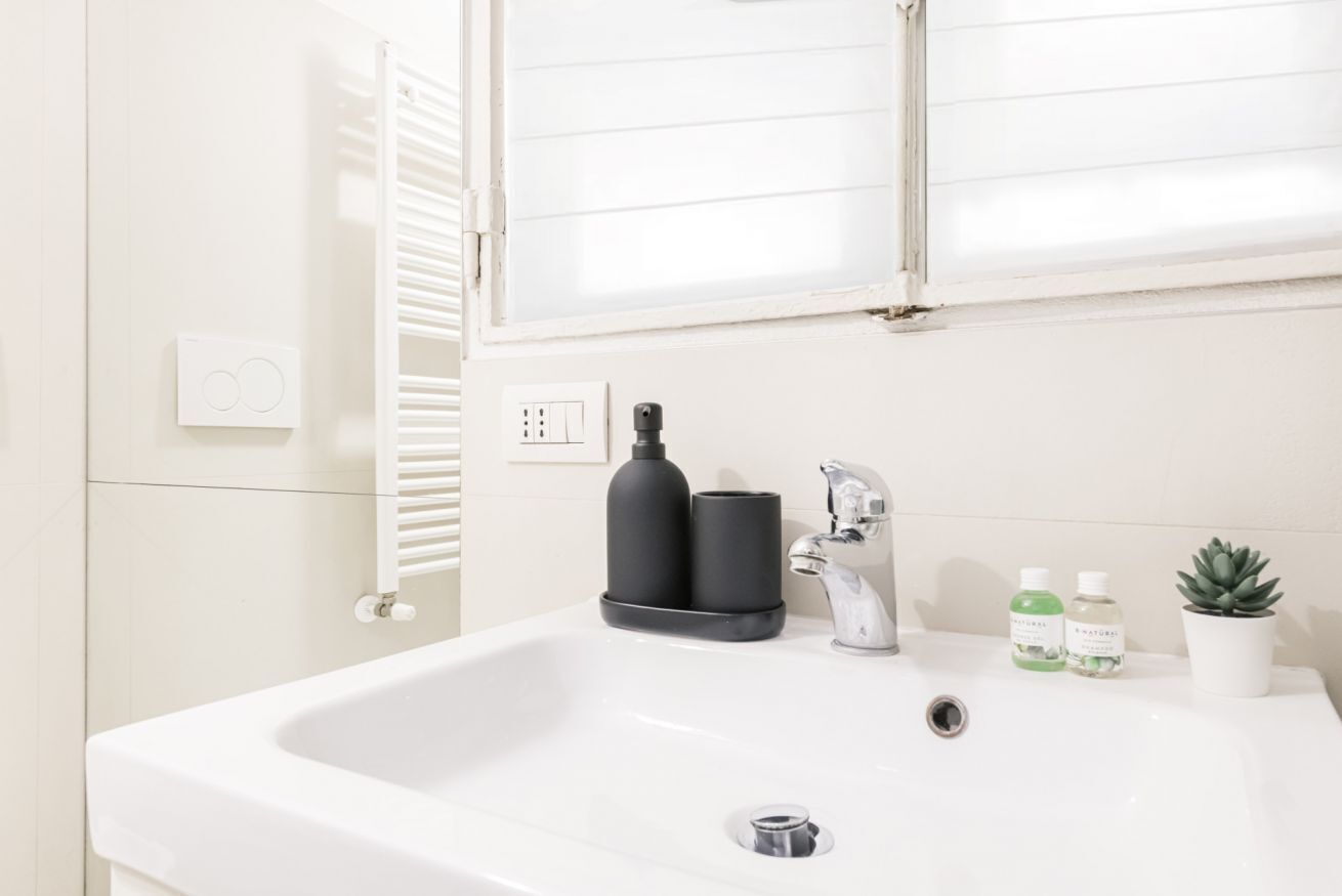 A white bathroom with a sink, faucet, and two bottles of liquid soap.