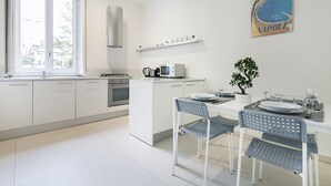 A modern kitchen with white cabinetry, a built-in oven, a microwave, and a gas stove. There is a window providing natural light, and a decorative poster on the wall. - Easylife - Classy apartment in Buenos Aires (Milano)