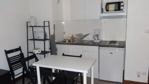 A compact kitchen with white cabinets, a microwave, a coffee maker, and a dishwasher. There is a dining table with chairs. - Studio in Grenoble city center (Grenoble)