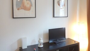 A room with a black TV on a stand, a white lamp, and two framed artworks on the wall. - Studio in Grenoble city center (Grenoble)